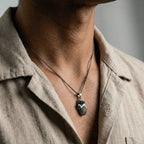 Person wearing a necklace with a heart pendant on a neutral background