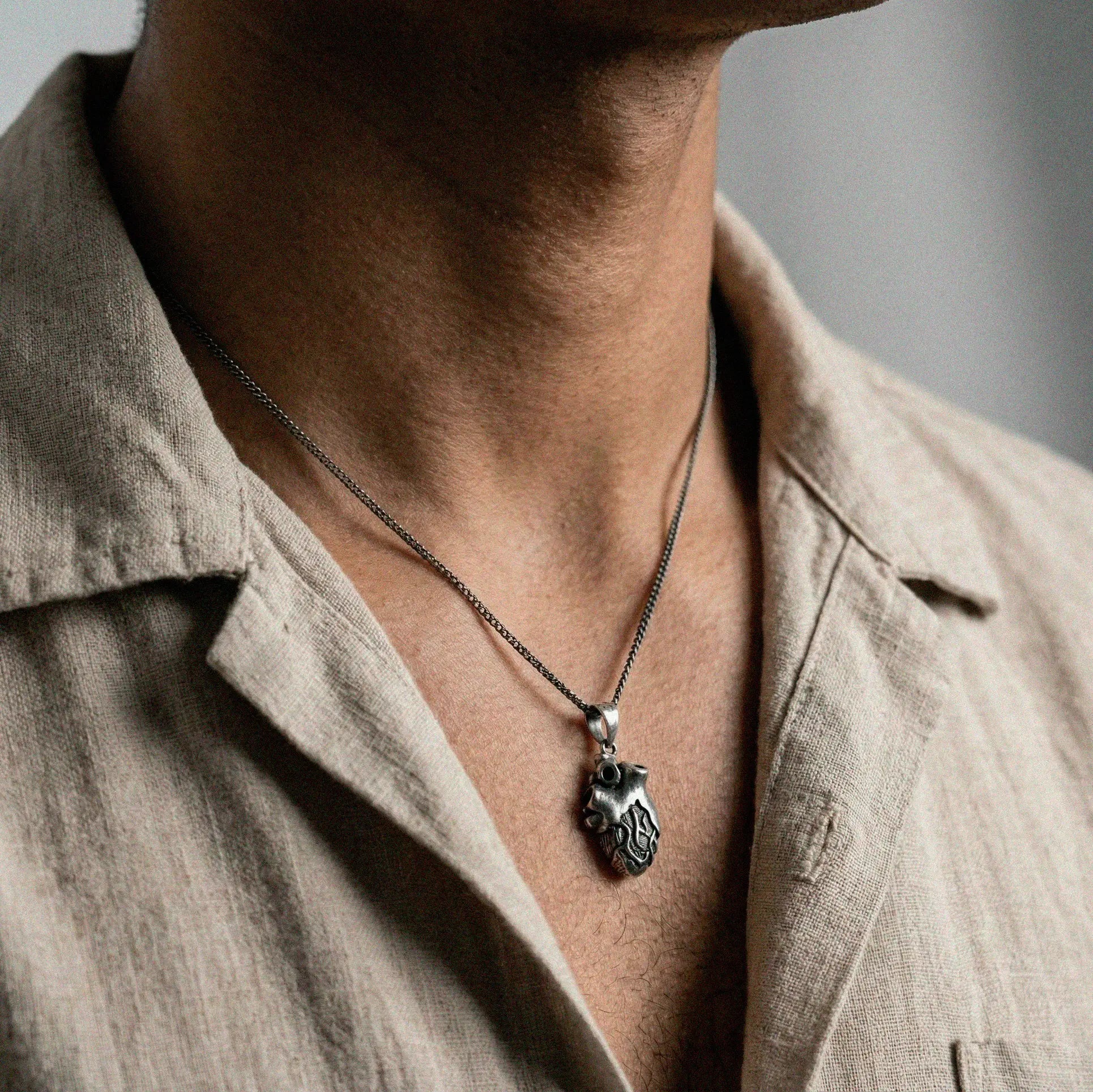 Person wearing a necklace with a heart pendant on a neutral background