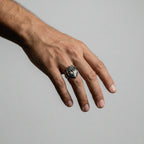 Hand wearing a silver ring with a heart design on a plain background