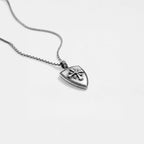 Silver necklace with a shield-shaped pendant on a light gray background
