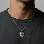 Person wearing a necklace with a shield-shaped pendant on a plain background