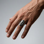 Hand wearing a silver medieval shield ring on a gray background