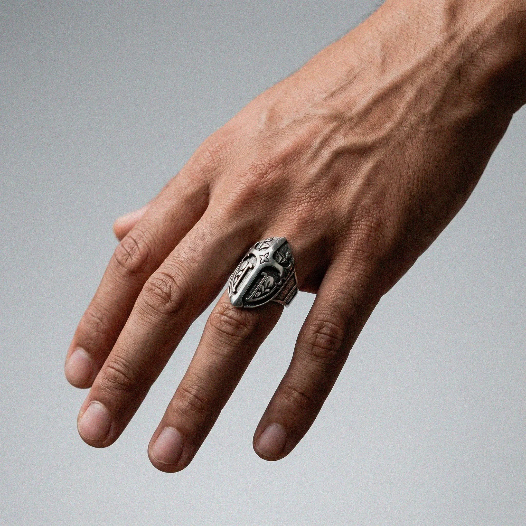 Hand wearing a silver medieval shield ring on a gray background