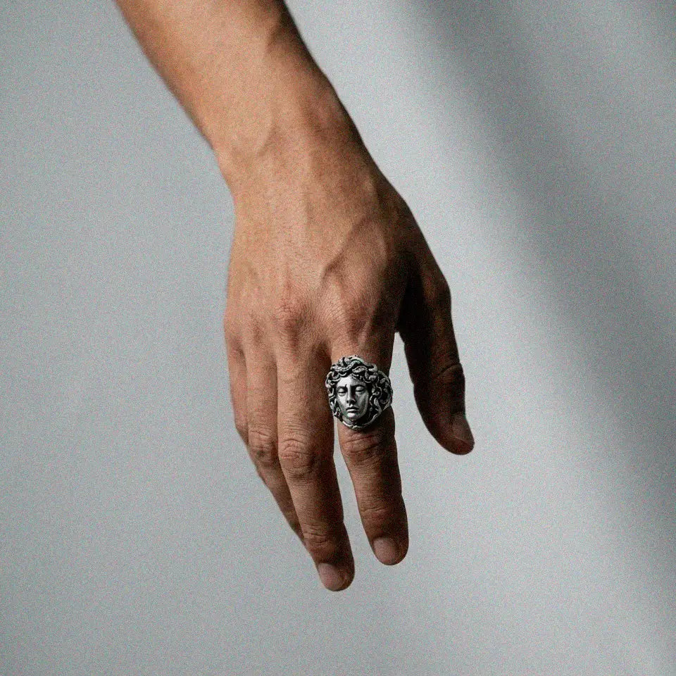 Hand wearing a silver ring with a medusa design on a gray background