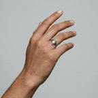 Hand wearing a silver ring with a pearl stone on a gray background