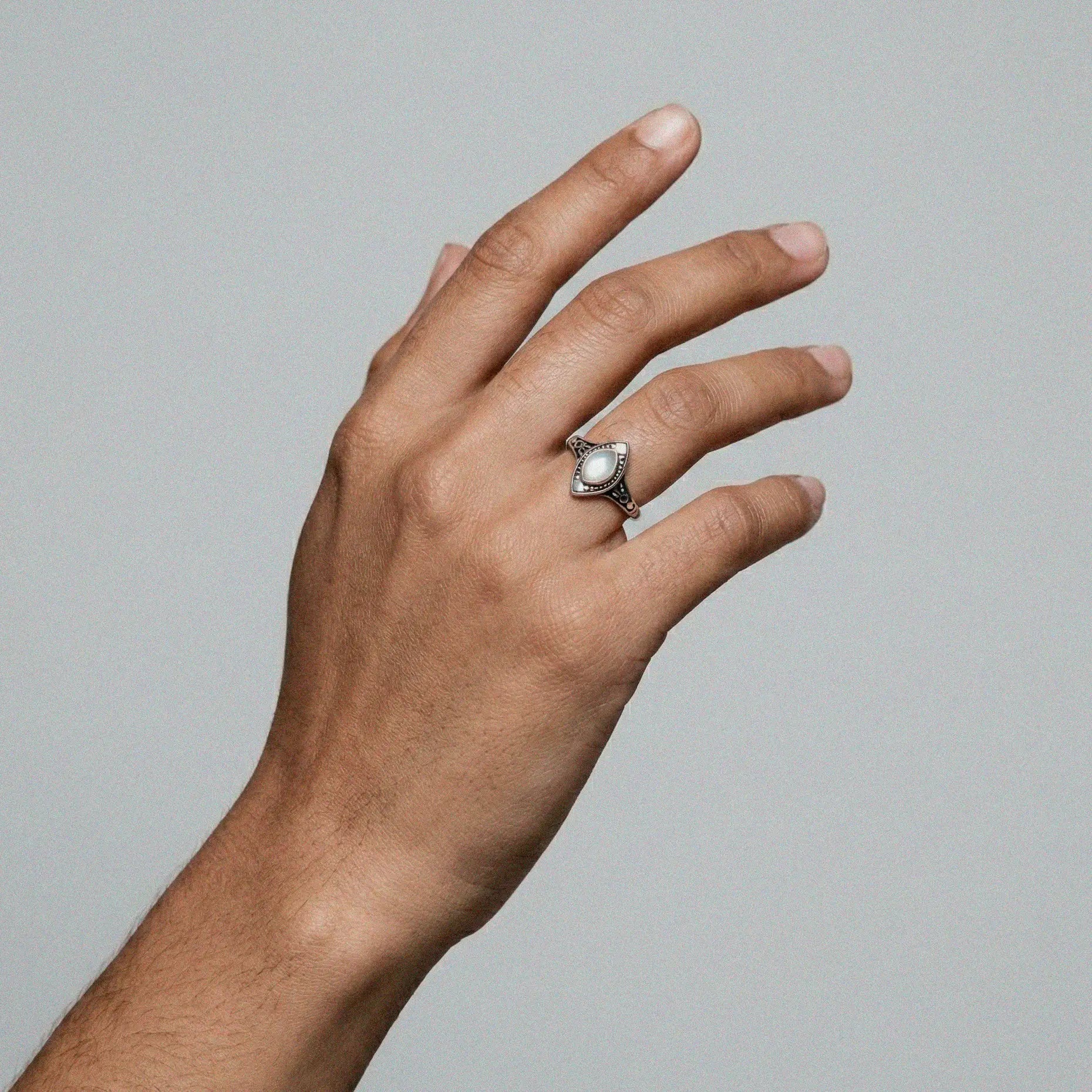 Hand wearing a silver ring with a pearl stone on a gray background