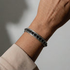 Silver bracelet with black stones on a wrist against a neutral background