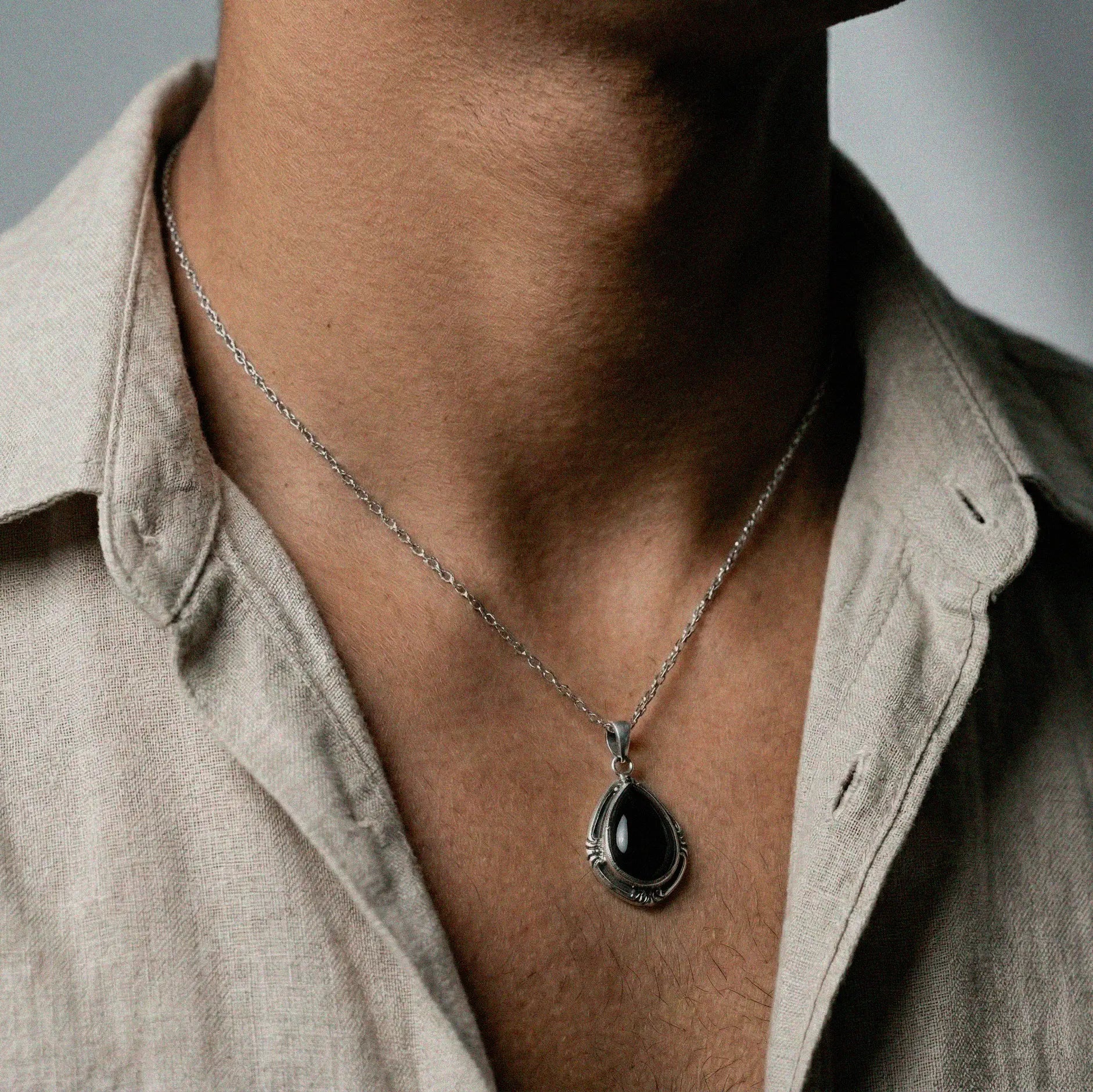 Necklace with a black pendant worn by a person in a beige shirt.