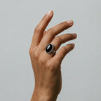 Hand wearing a ring with an obsidian stone on a neutral background