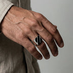 Hand wearing a silver ring with an obsidian stripes design on a neutral background