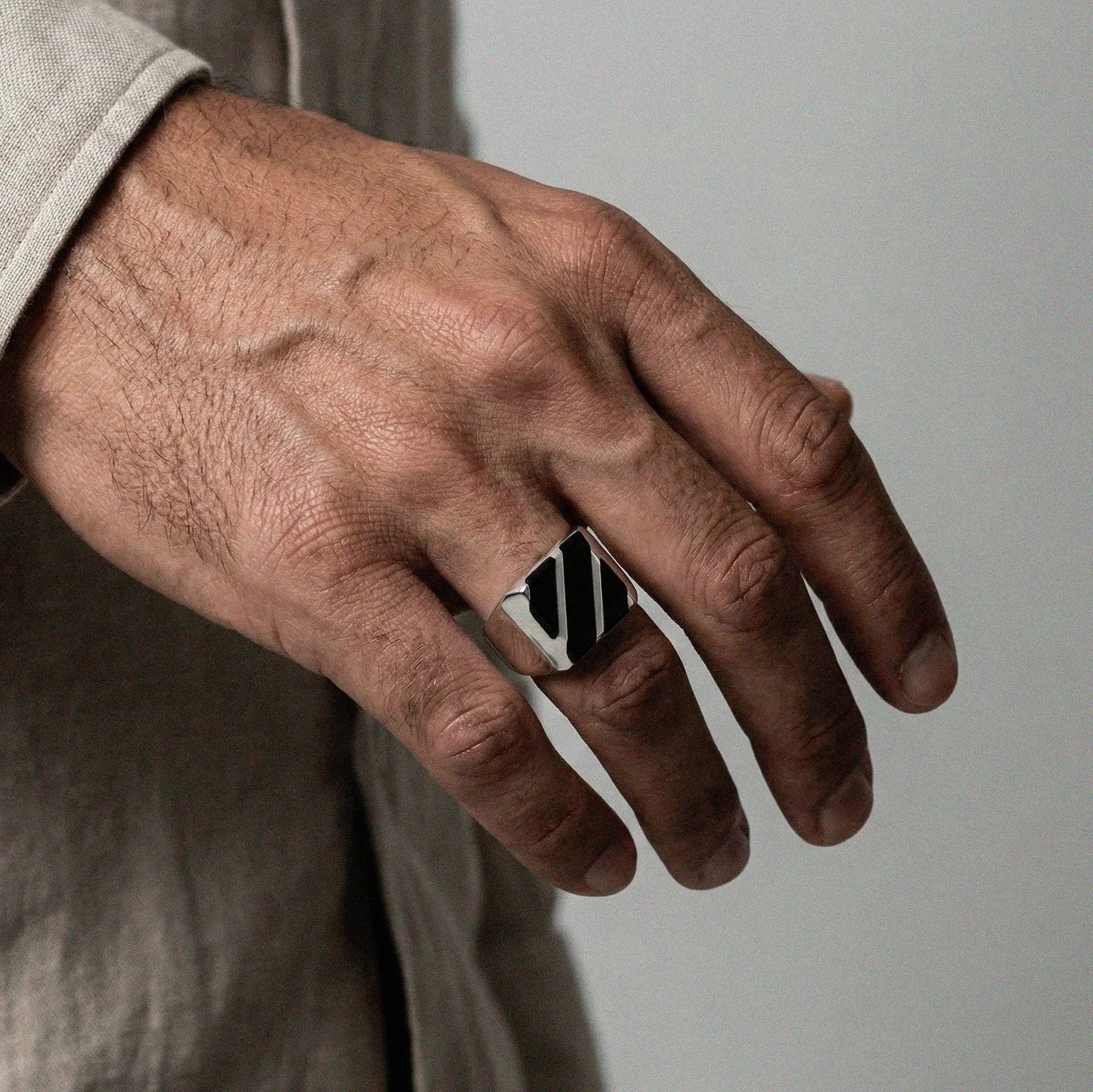 Hand wearing a silver ring with an obsidian stripes design on a neutral background