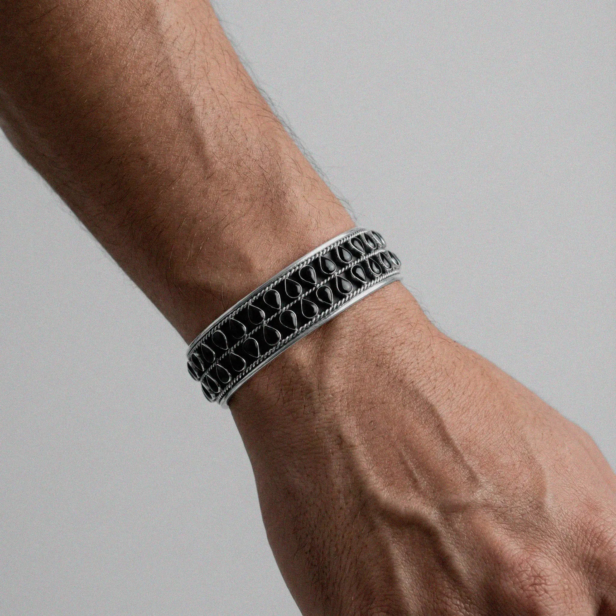 Close-up of a wrist wearing an obsidian silver bracelet on a gray background