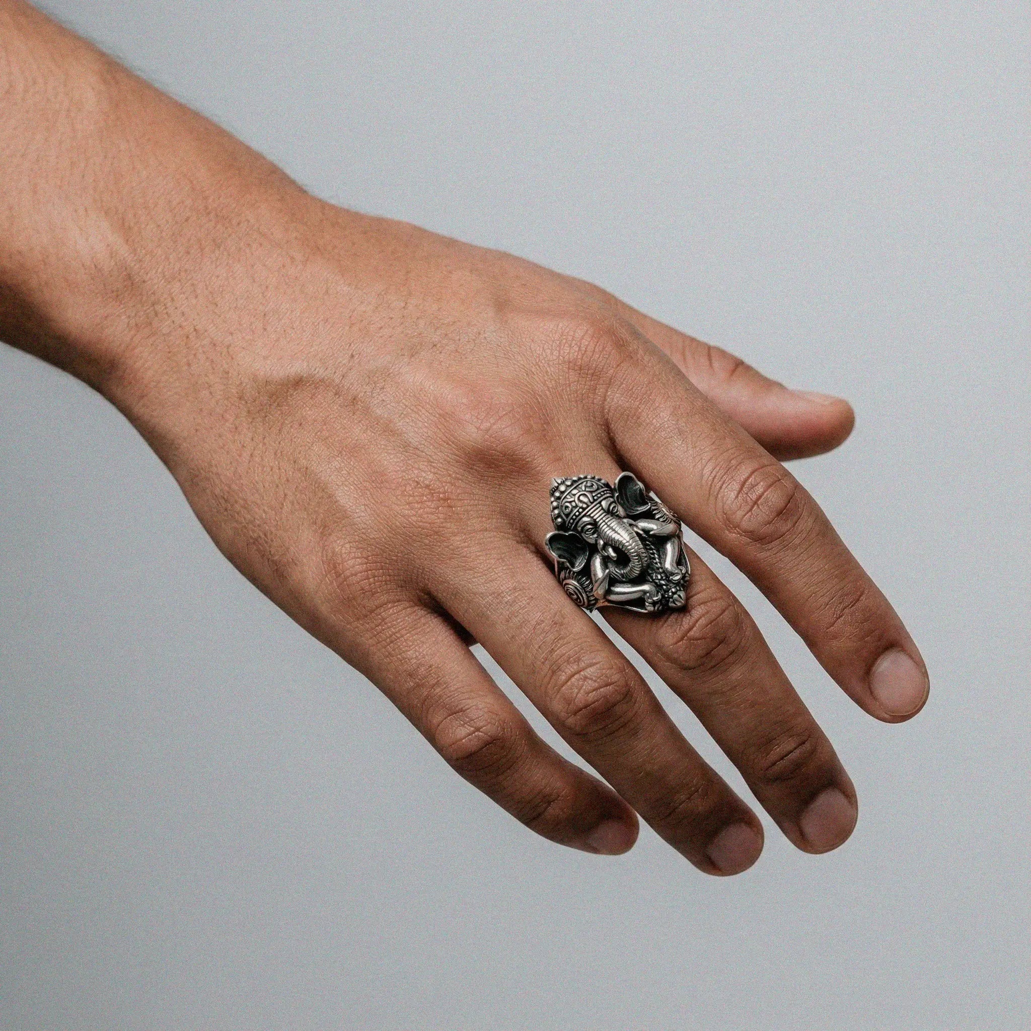 Hand wearing a silver ring with ganesha design on a gray background