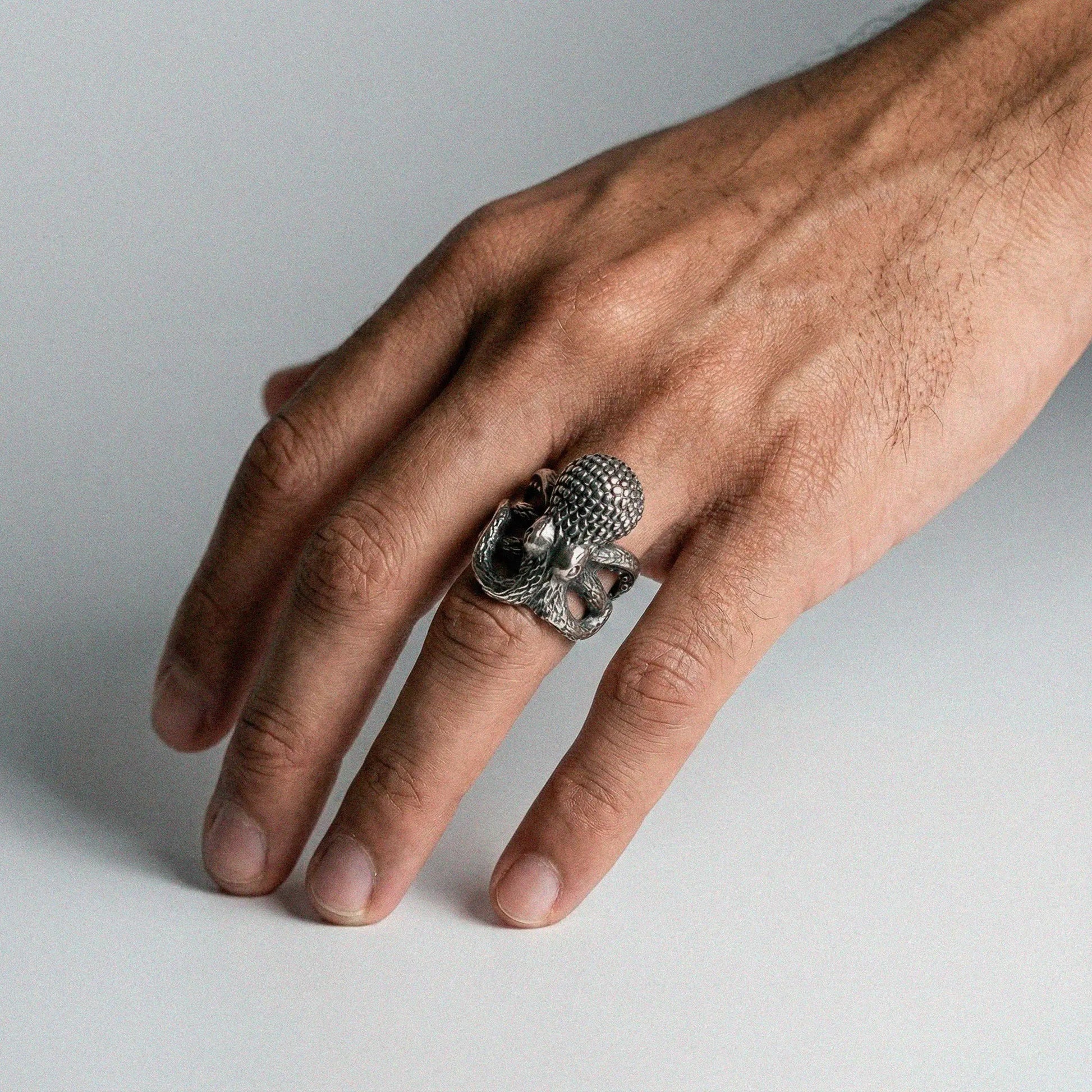 Hand wearing a silver ring with an octopus design on a light gray background