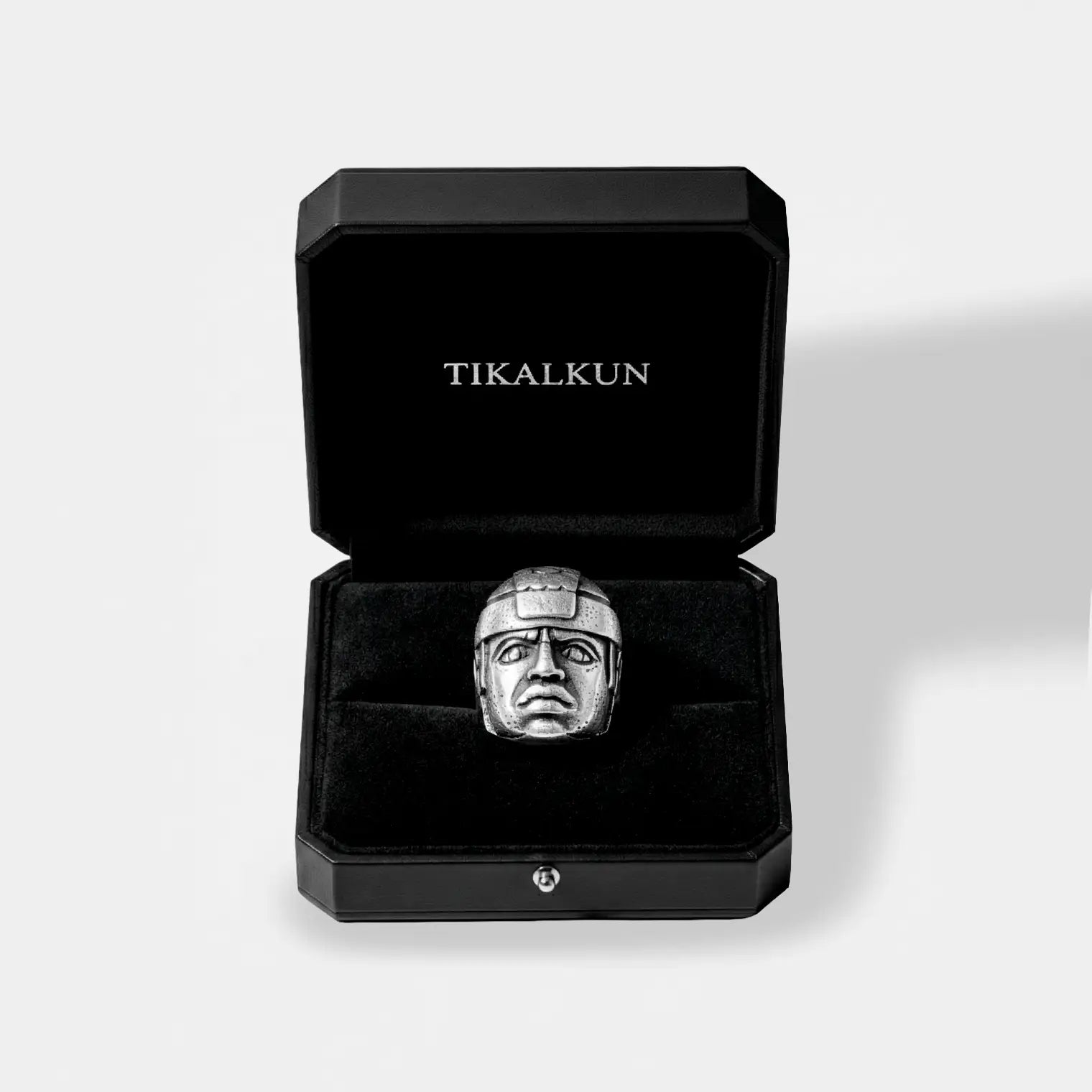 Black jewelry box with 'TIKALKUN' branding containing a silver olmec head ring