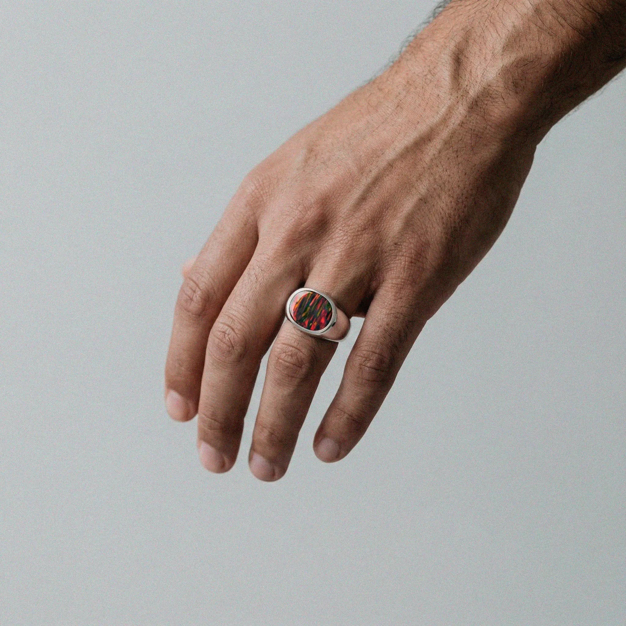 Hand wearing a ring with an opal fire stone on a gray background