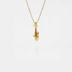 Gold orca pendant necklace on a thin chain against a light gray background