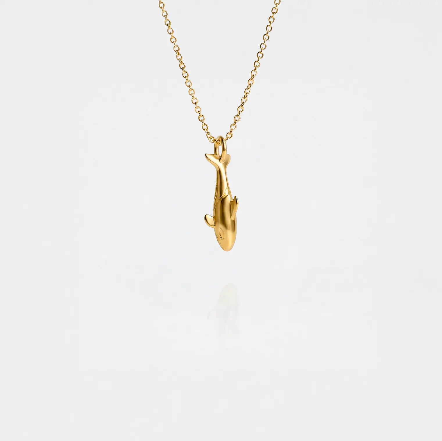 Gold orca pendant necklace on a thin chain against a light gray background