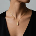 Gold orca necklace with a pendant on a person wearing a black top against a neutral background
