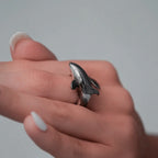 Hand wearing a silver orca-shaped ring on a plain background