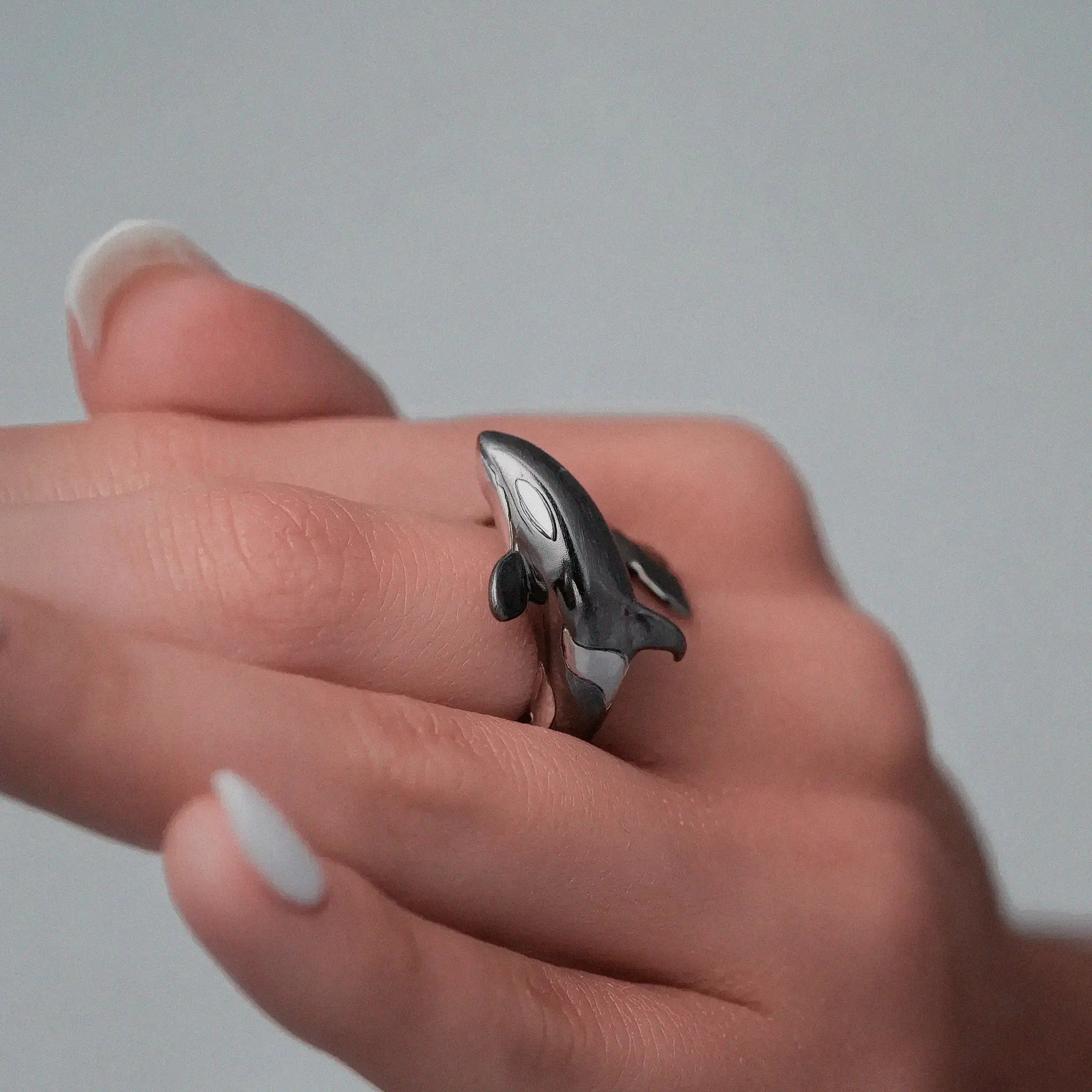 Hand wearing a silver orca-shaped ring on a plain background