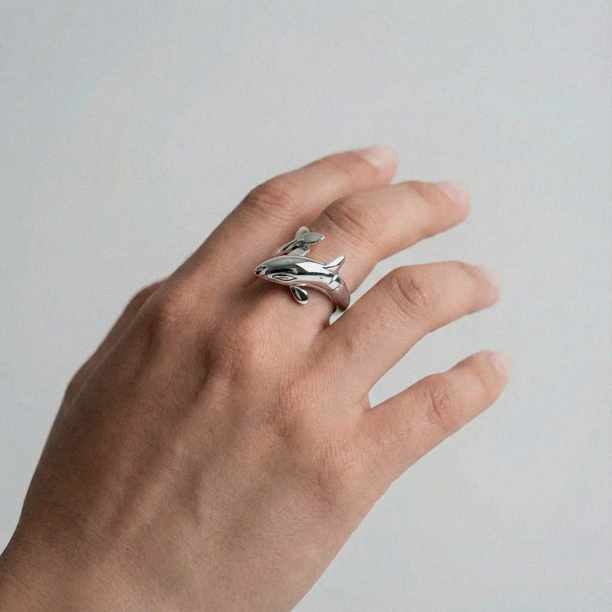 Hand wearing a silver orca ring on a plain background