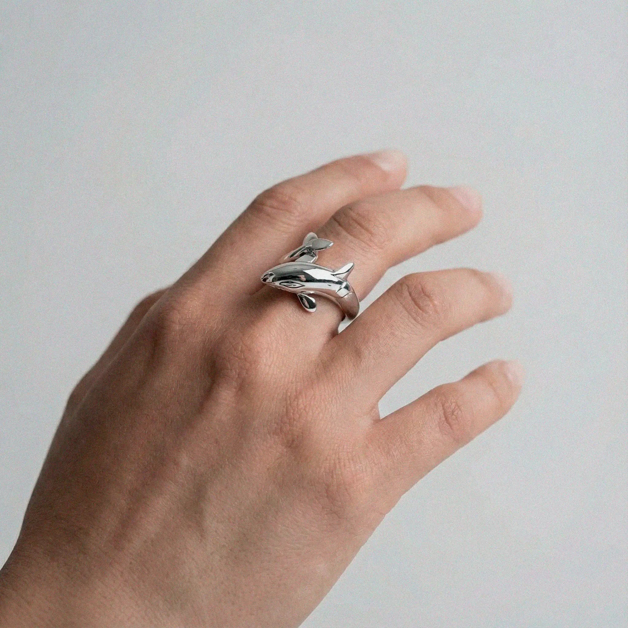 Hand wearing a silver orca ring on a plain background
