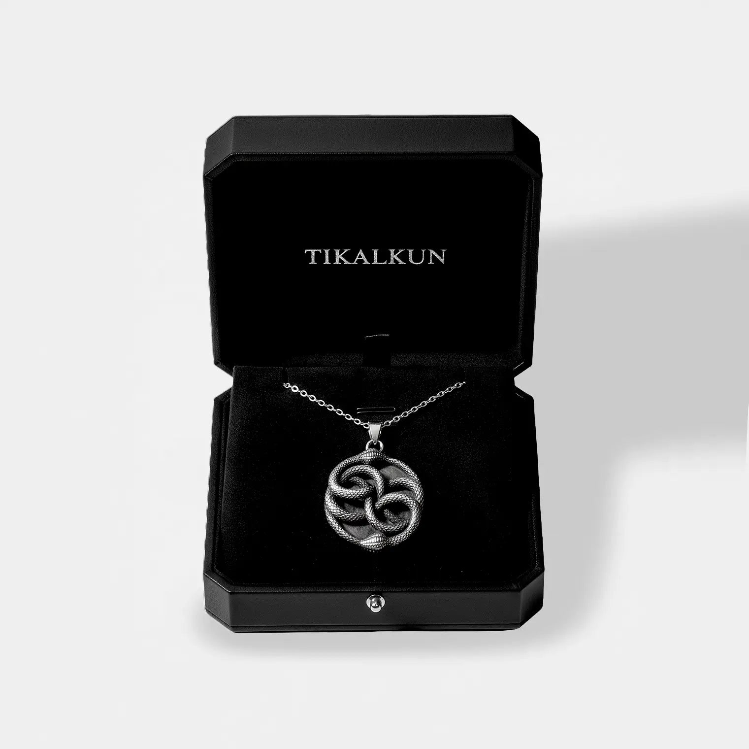 Silver necklace with an ouroboros pendant in an open black Tikalkun jewelry box on a light gray background