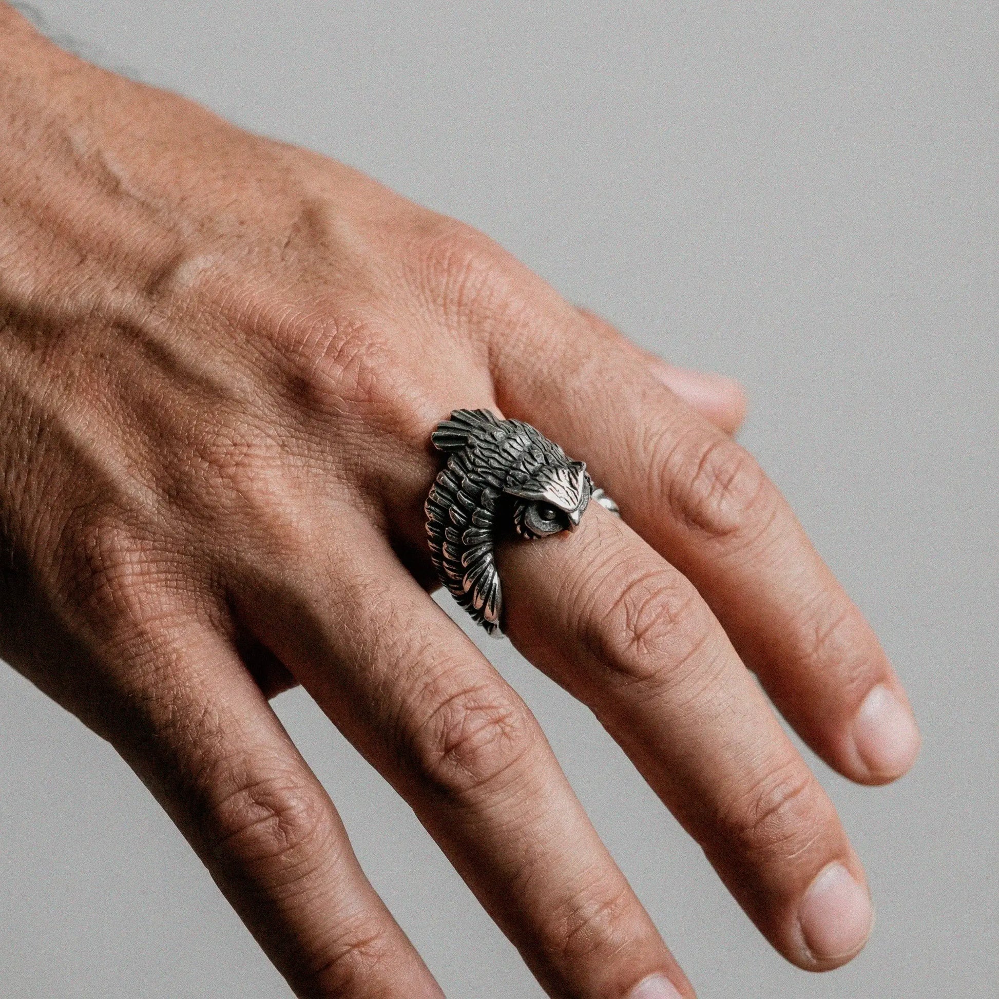 person´s hand wearing an owl silver ring on a gray background