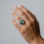 Hand wearing a ring with a labradorite gemstone on a neutral background
