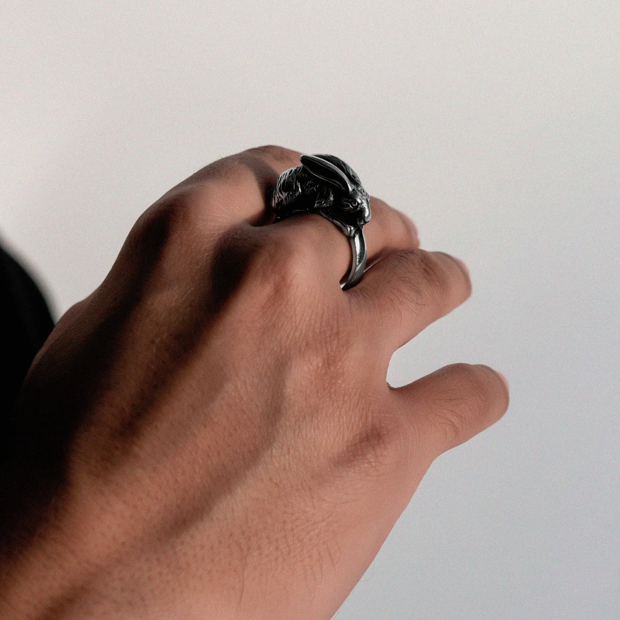 Hand wearing a silver RABBIT ring with a detailed design on a plain background