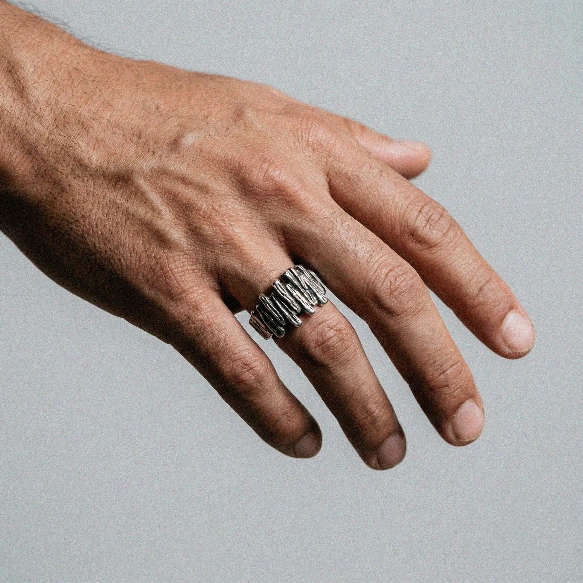 Hand wearing a silver ring on a gray background