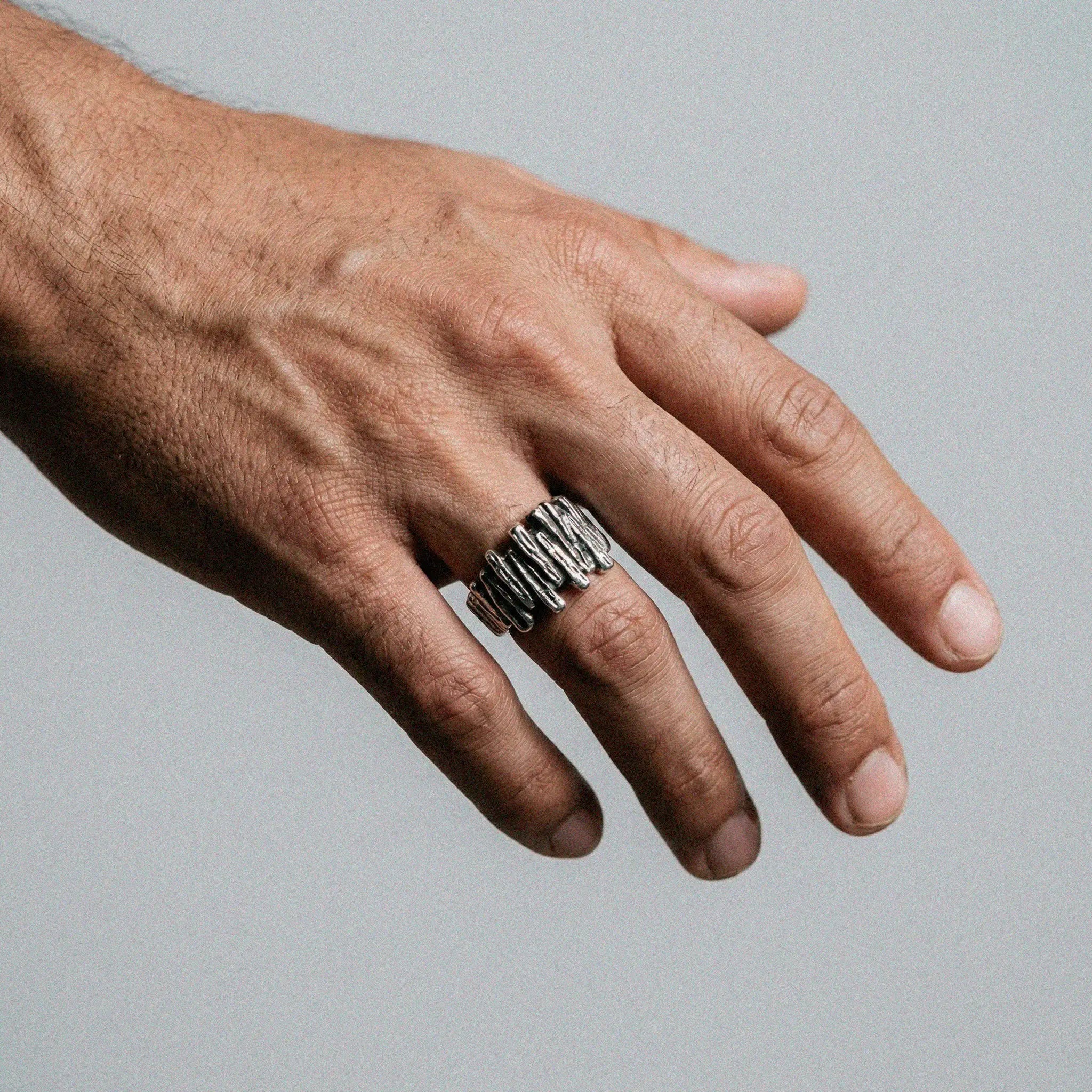 Hand wearing a silver ring on a gray background