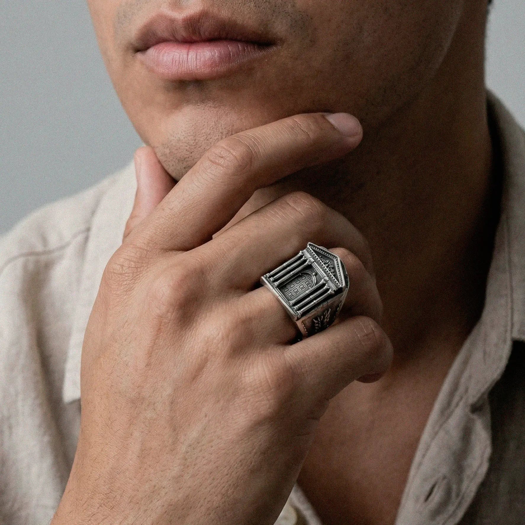 Man wearing a silver ring with a roman door design, touching his chin.