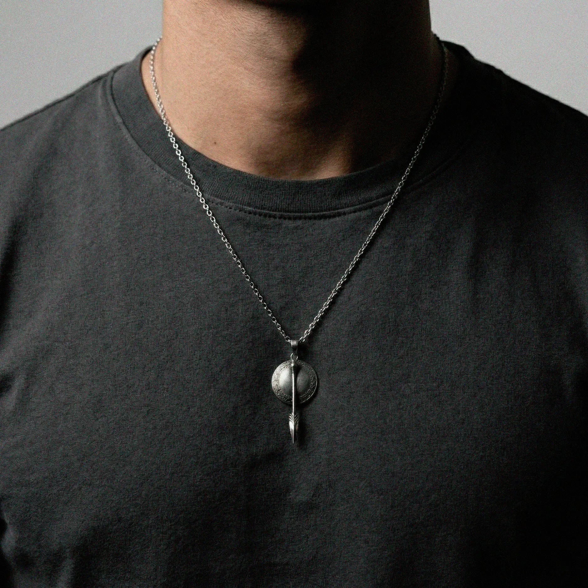 Person wearing a necklace featuring a Roman shield and spear pendant.