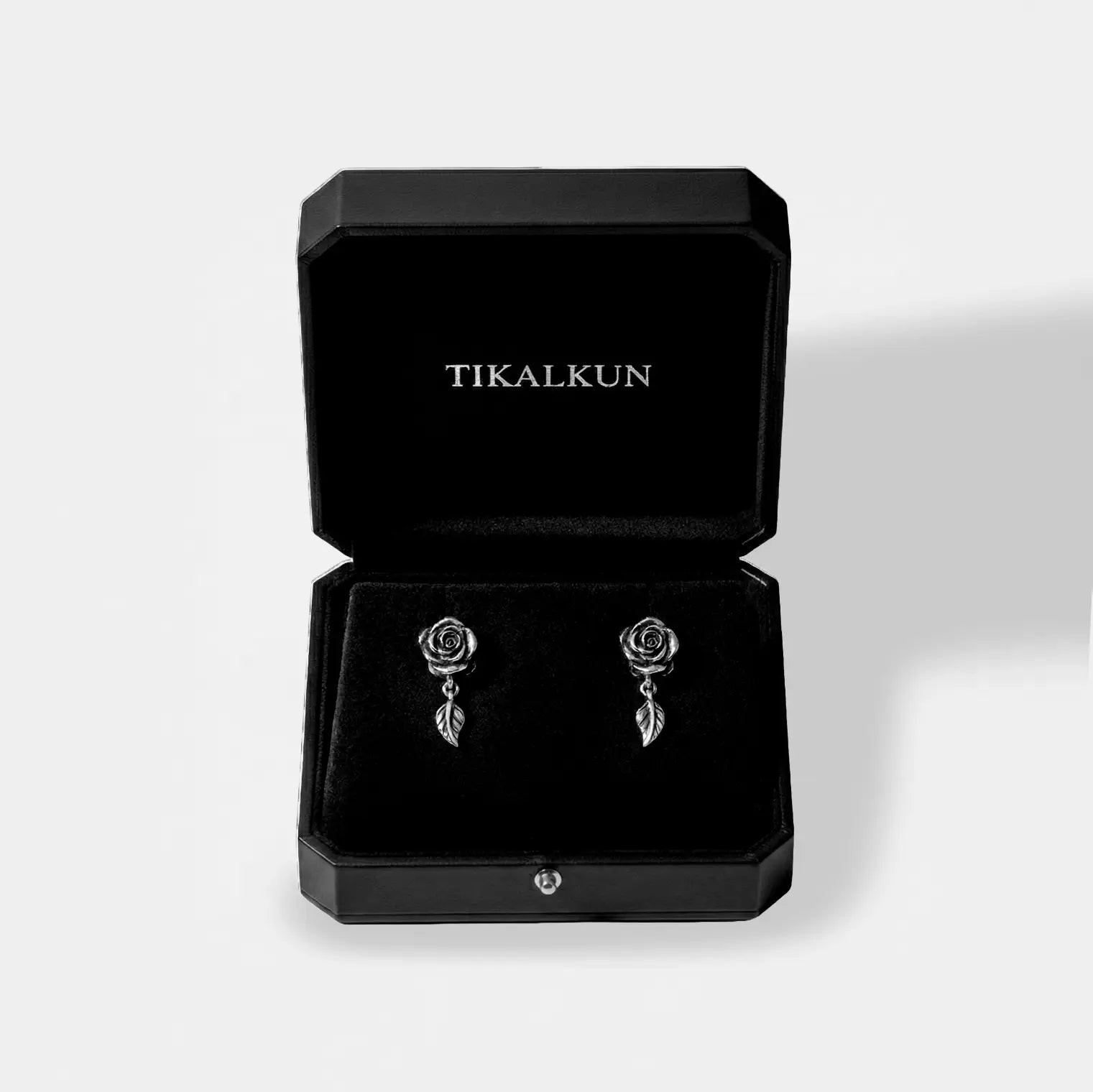 Rose-shaped earrings in a black Tikalkun box on a light gray background