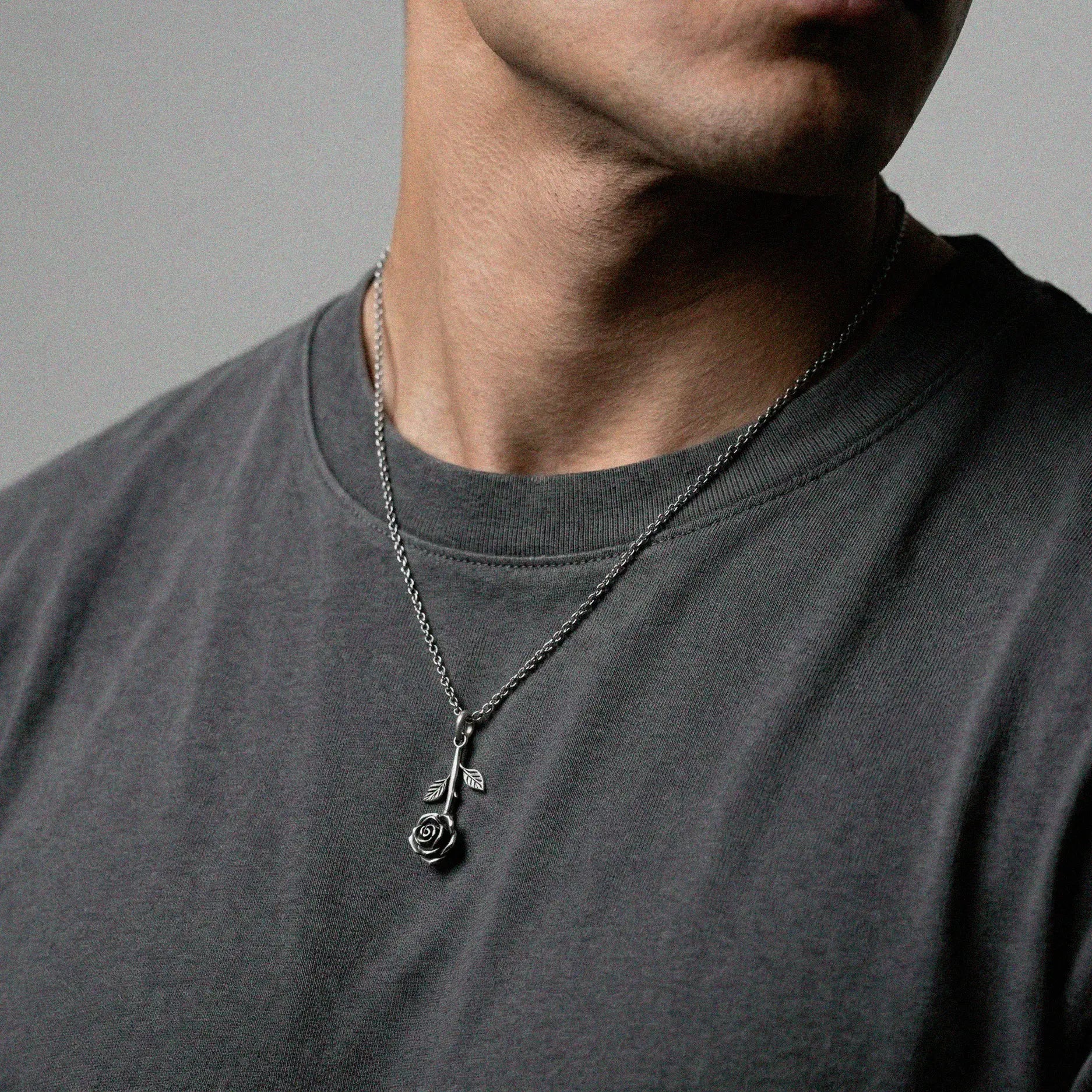 Person wearing a necklace with a rose pendant on a gray background