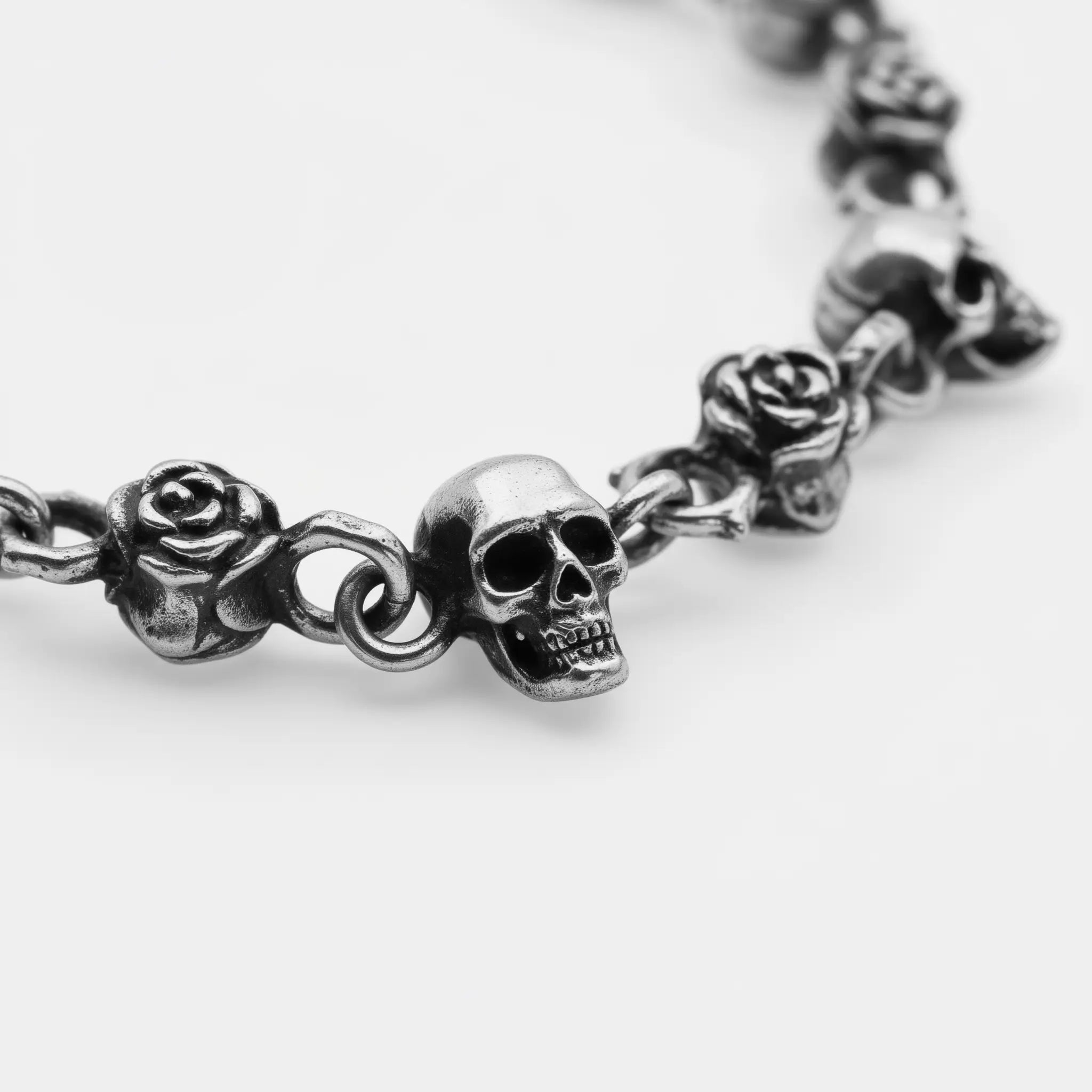 Silver necklace with skull and rose designs on a white background