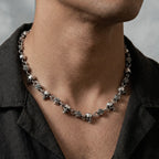 Close-up of a person wearing a silver necklace with skull and flower designs.