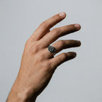 Hand wearing a silver rose-shaped ring on a plain background