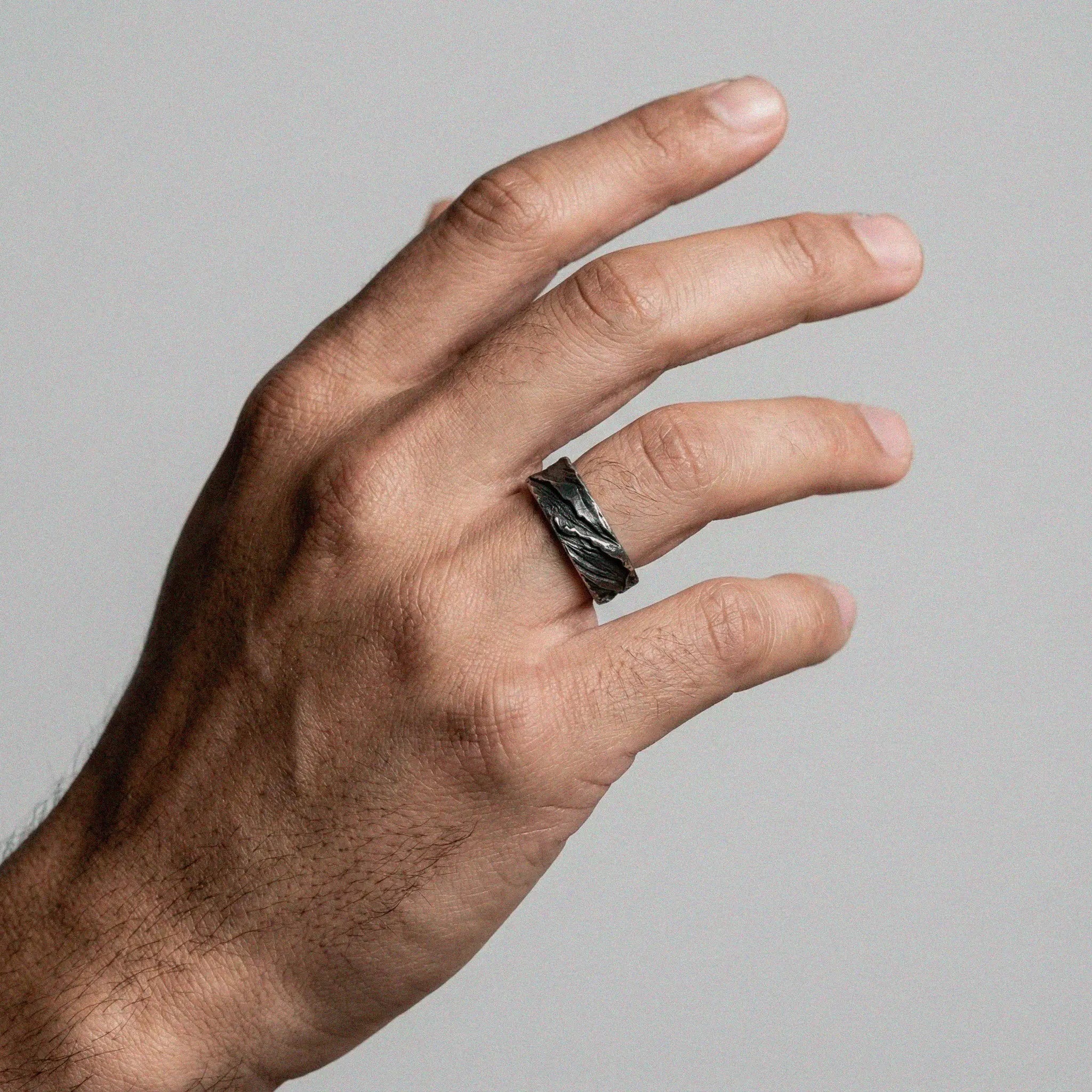Hand wearing a rustic ring on a plain background
