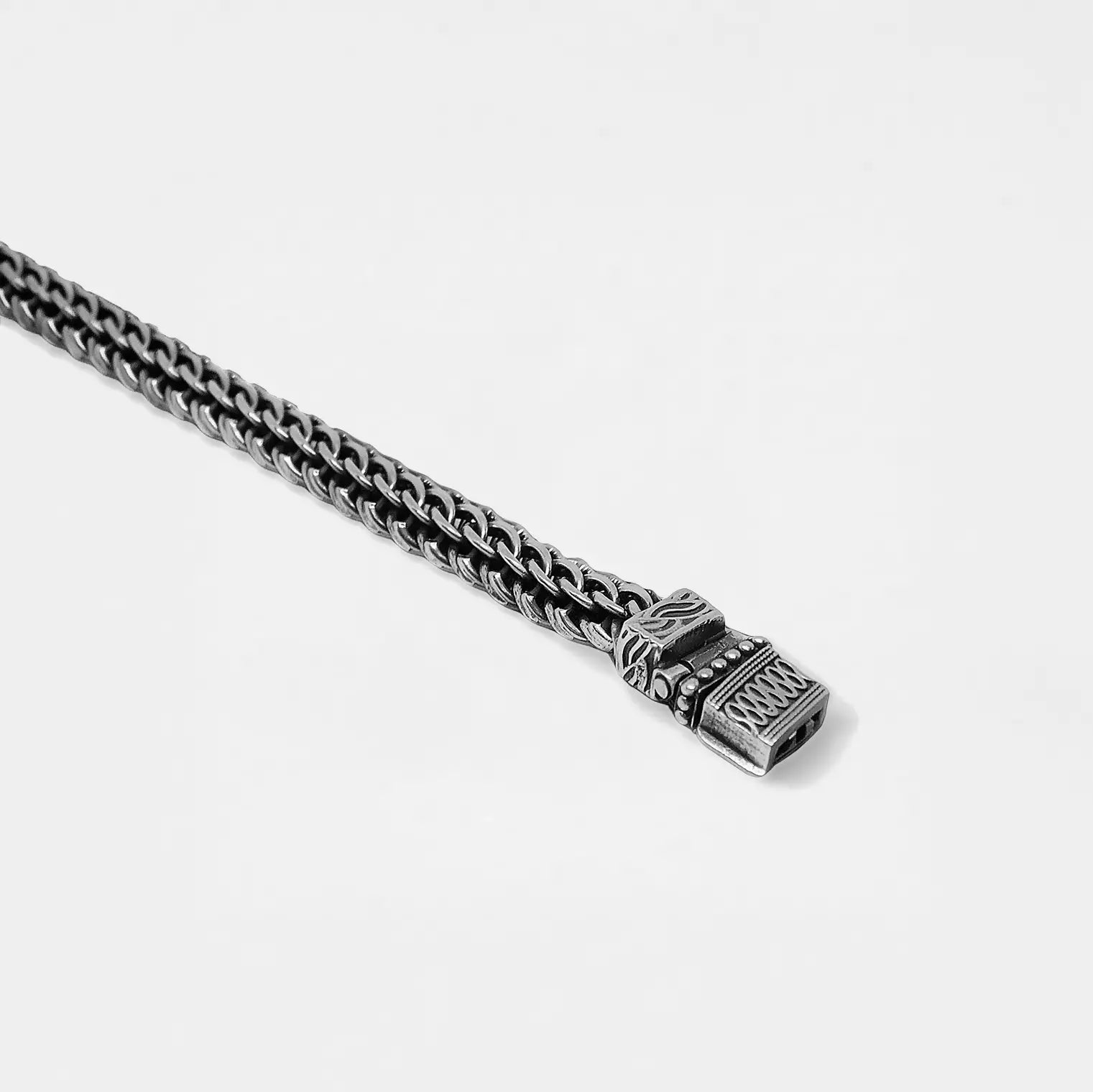 Close-up of a silver chain with a detailed clasp on a light gray background