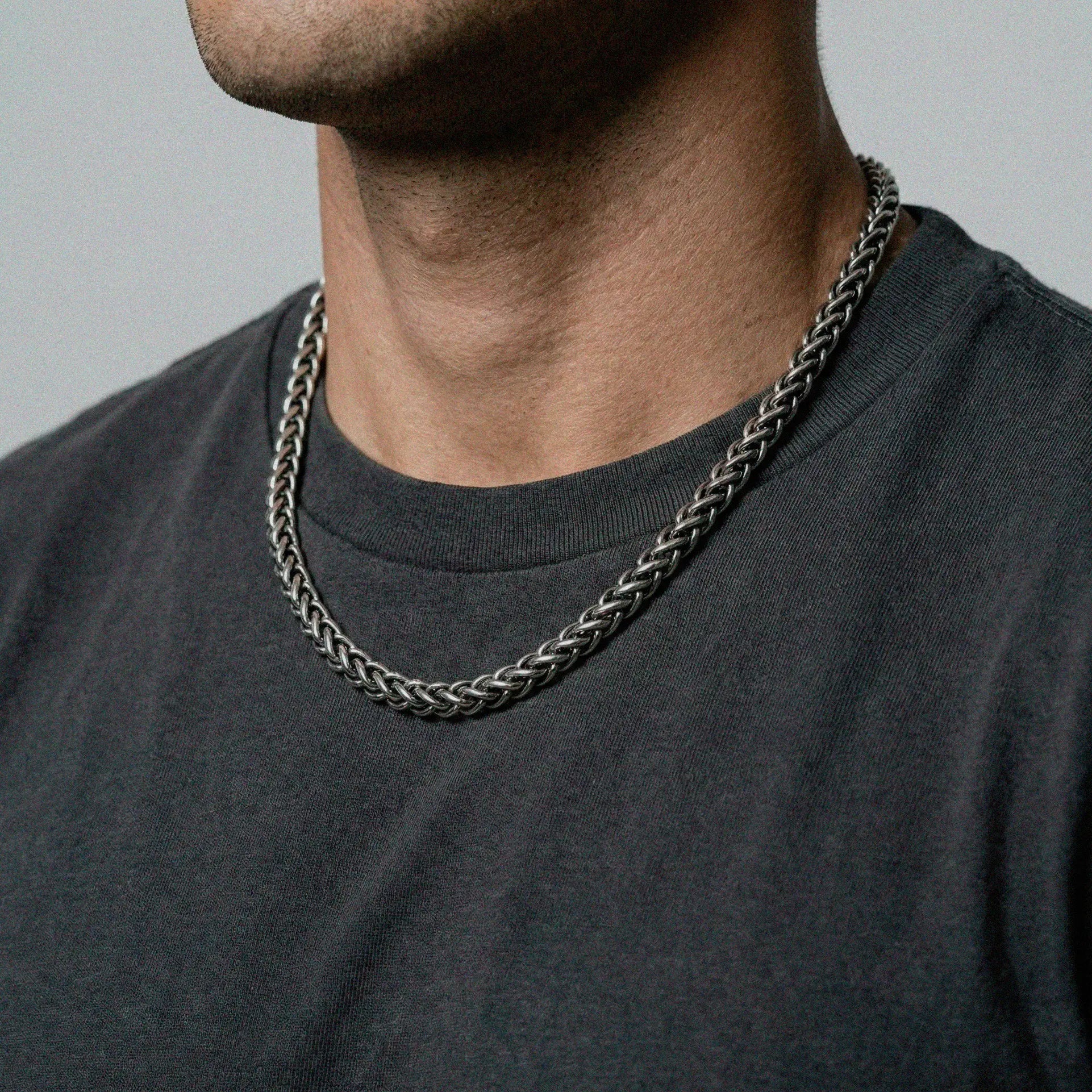 Person wearing a silver chain necklace on a plain background