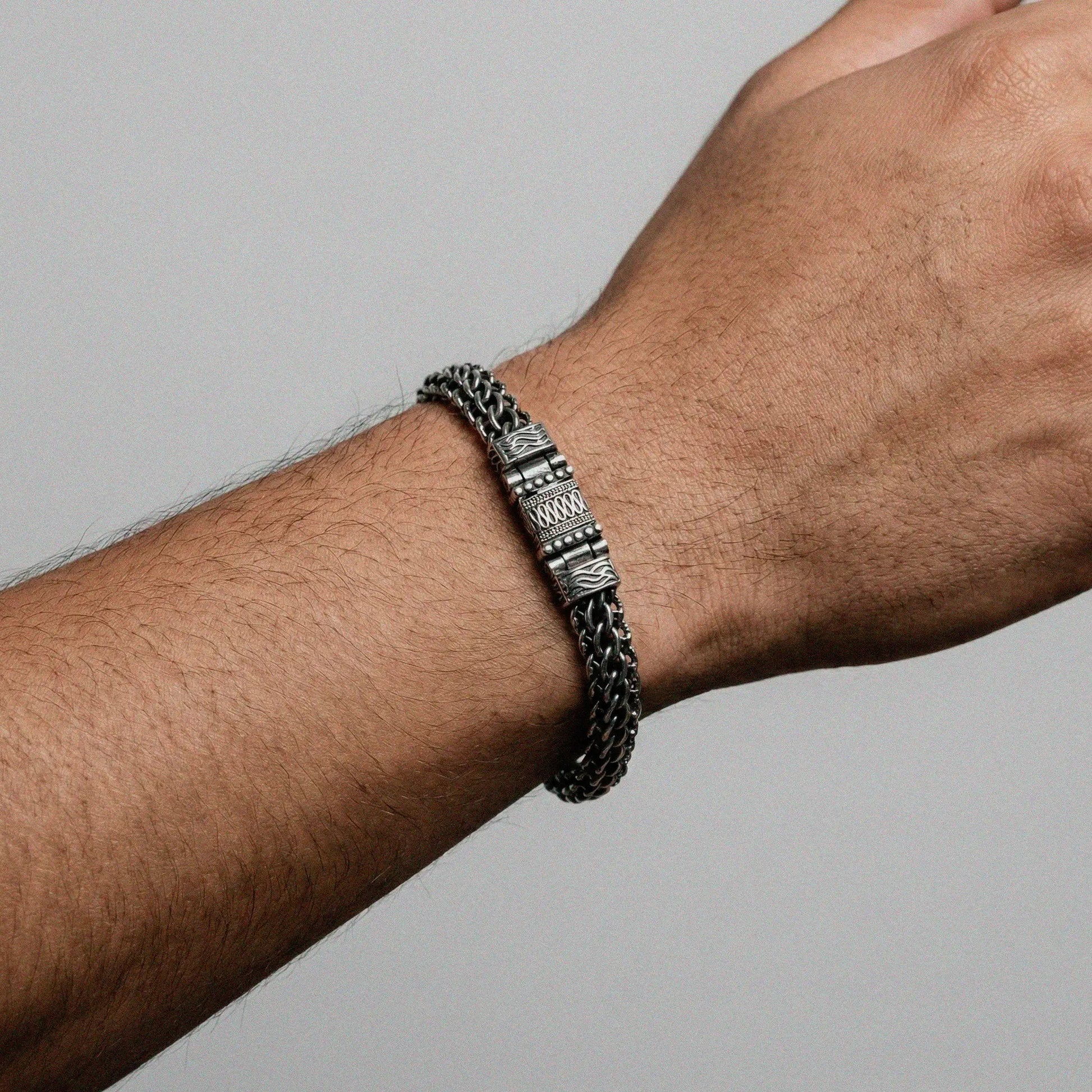 Silver bracelet on a wrist against a gray background