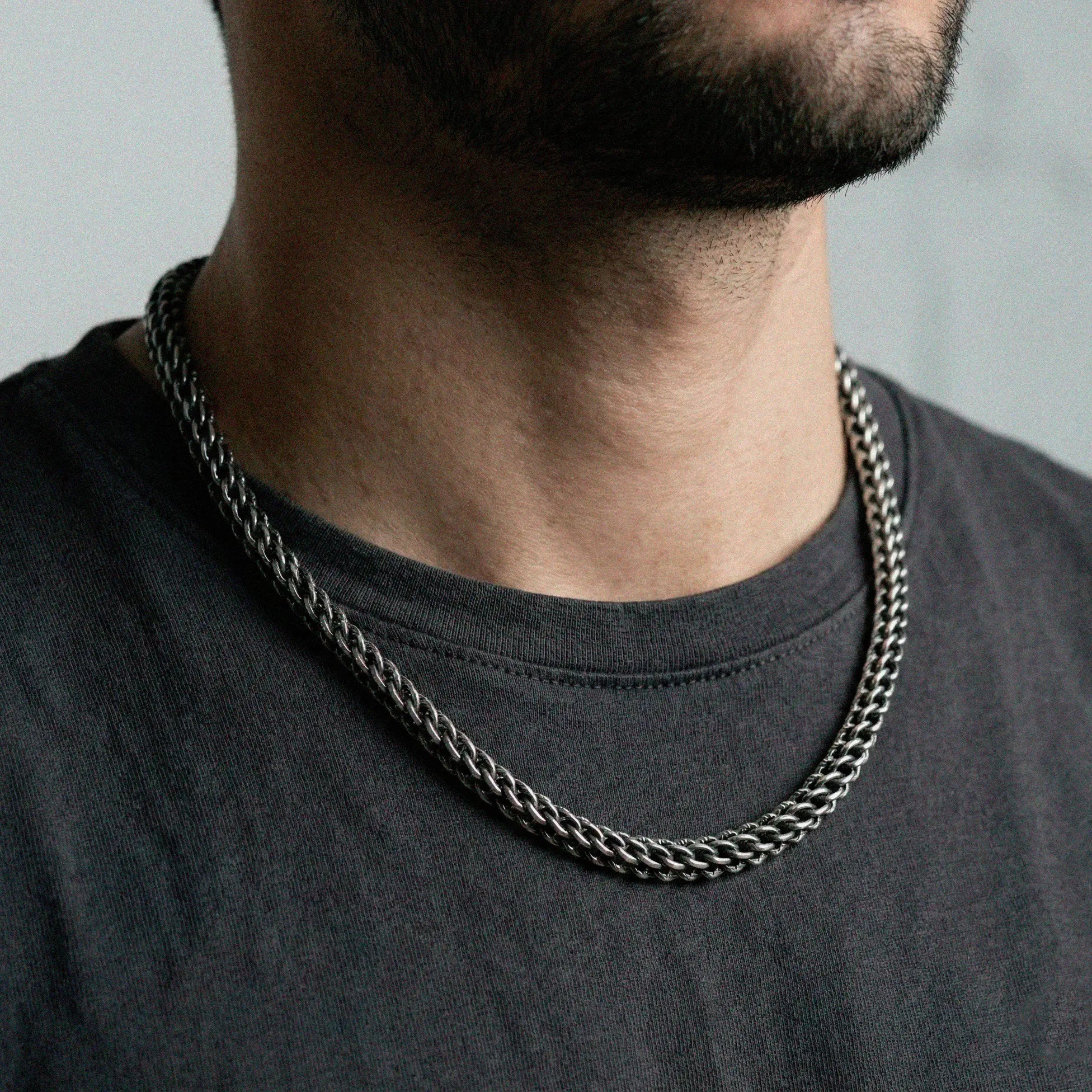 Man wearing a silver chain necklace against a neutral background