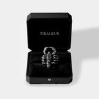 Scorpion-shaped ring in a black box with 'TIKALKUN' branding on a light gray background