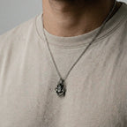 Person wearing a silver necklace with a scorpion pendant on a plain background