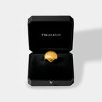 Gold shell-shaped ring in a black Tikalkun box on a light gray background