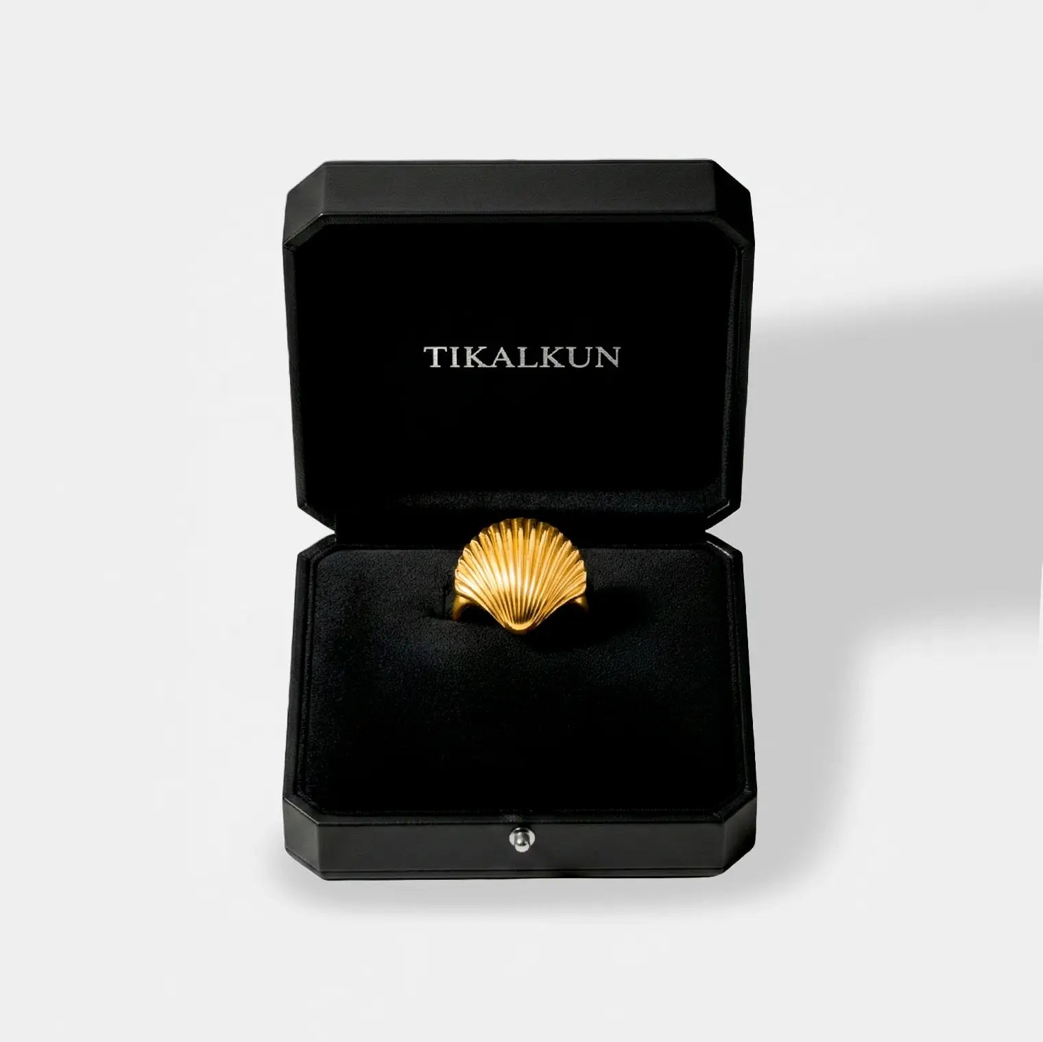 Gold shell-shaped ring in a black Tikalkun box on a light gray background