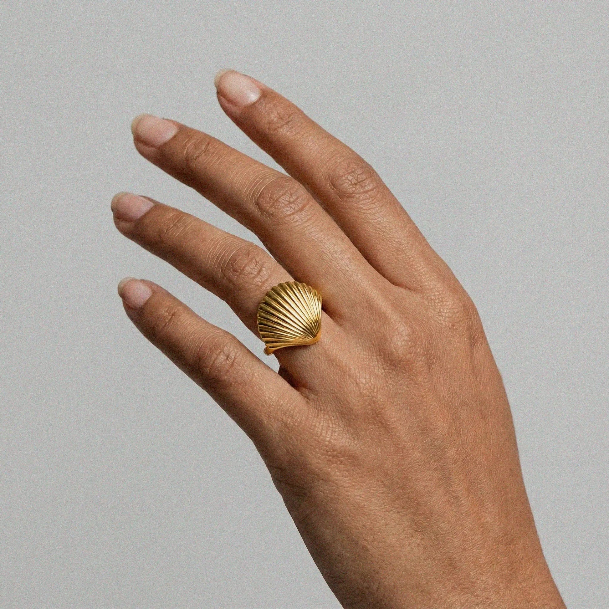 Hand wearing a gold shell-shaped ring on a plain background
